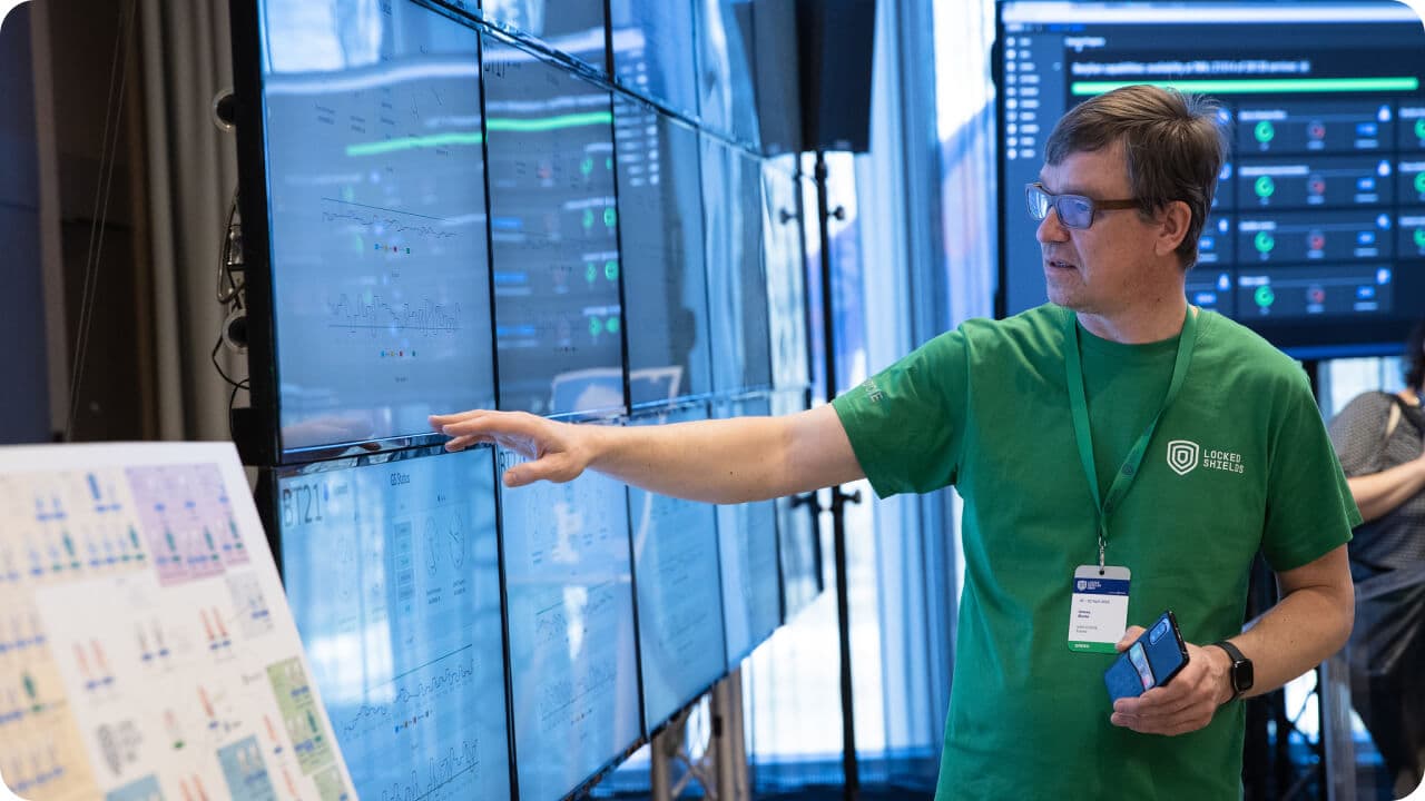 Man with badge and glasses in front of computer screens