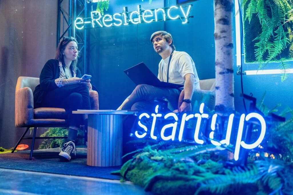Two people talking at Latitude59 surrounded by e-Residency and startup neon signs
