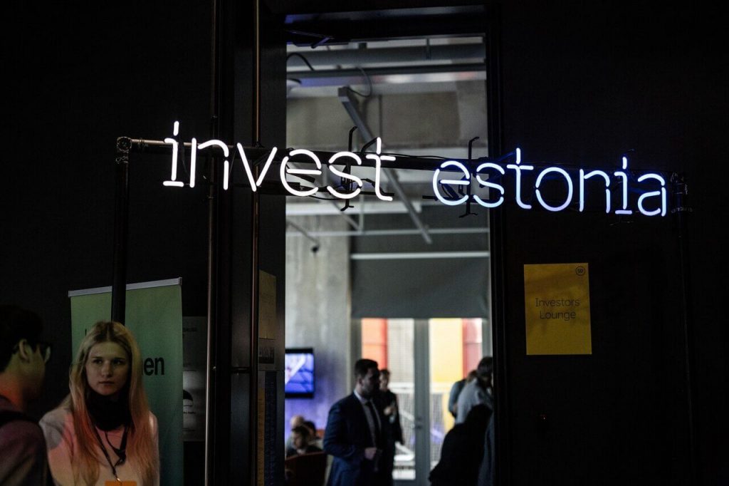 People at an investing conference in front of a neon sign Invest Estonia