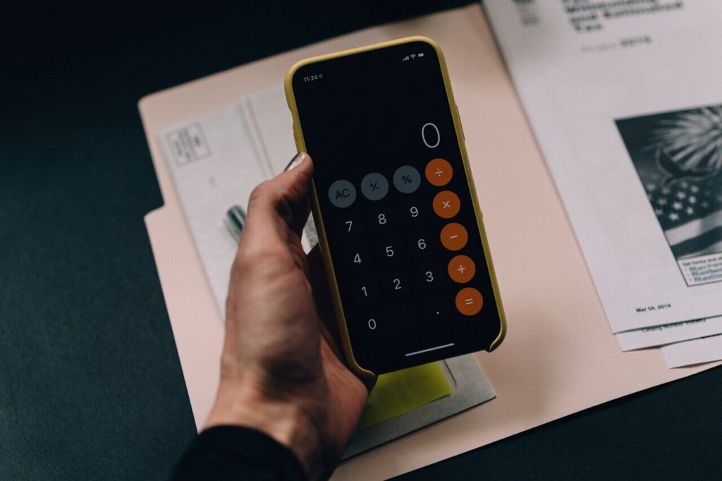 Hand holding a calculator above a folder of tax forms