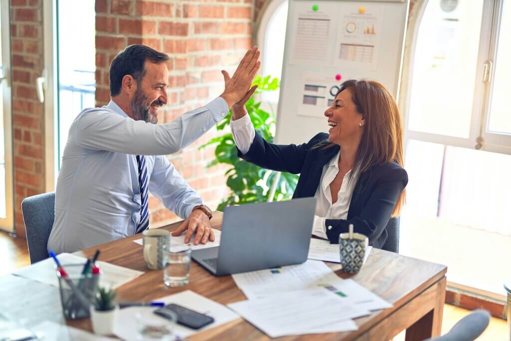 Man and woman high fiving over integrated PR and Advertising strategy in office state