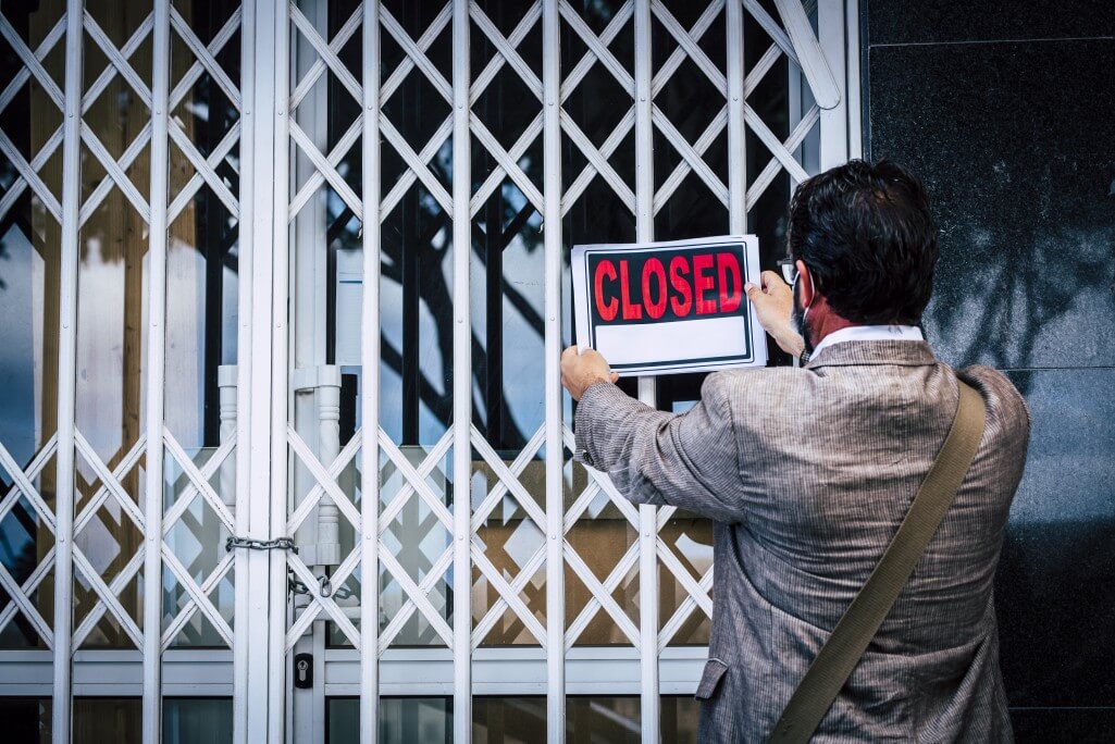 Close a company in Estonia: Rear view of businessman putting closed sign on display on locked shop or office